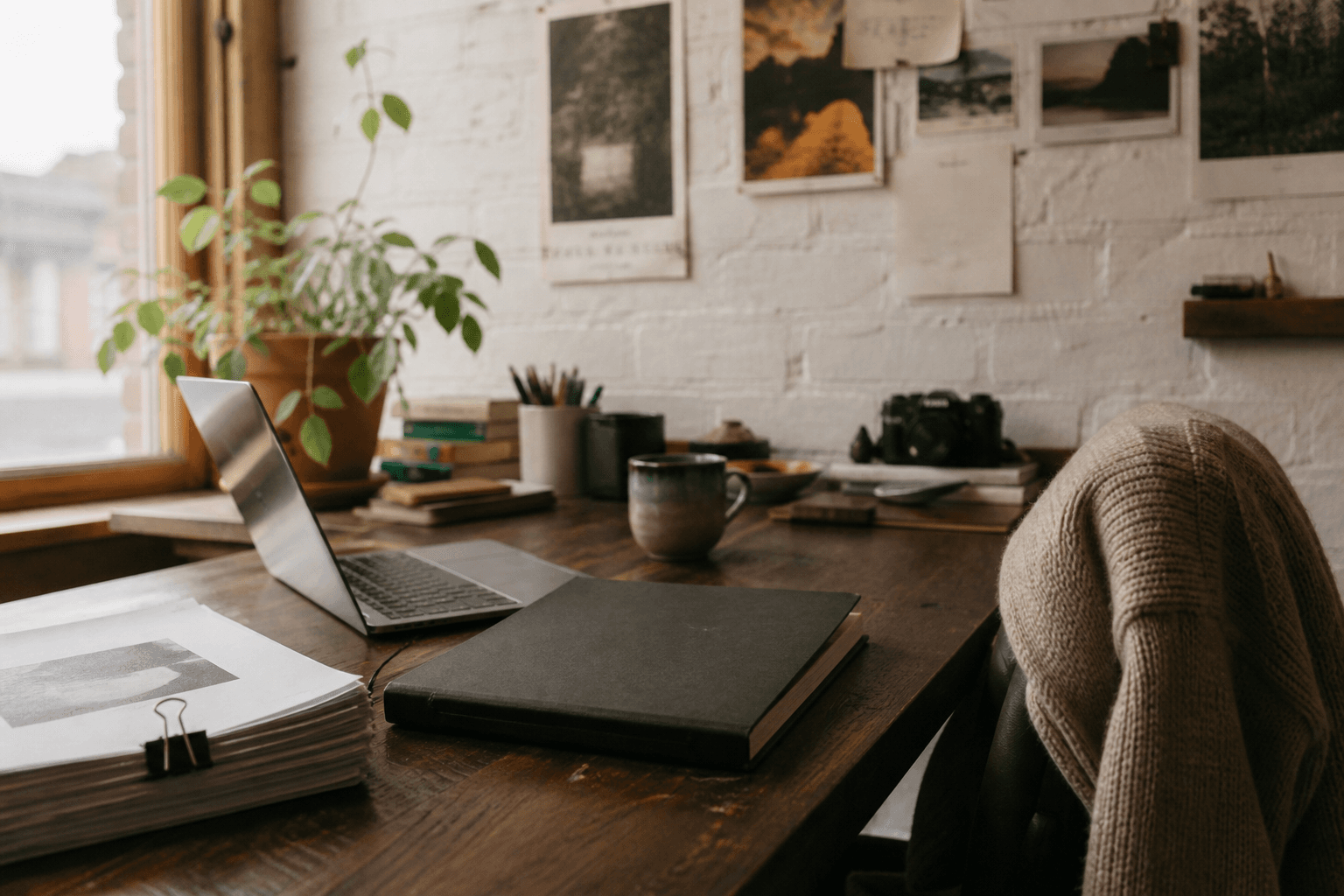Laptop, printed brief, and coffee on a wooden studio desk